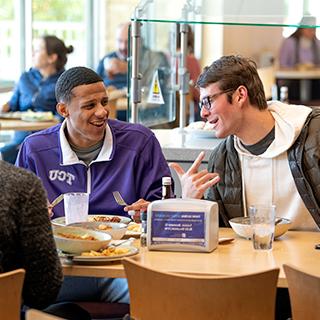 Two male TCU students share a laugh over lunch at the campus main dining hall